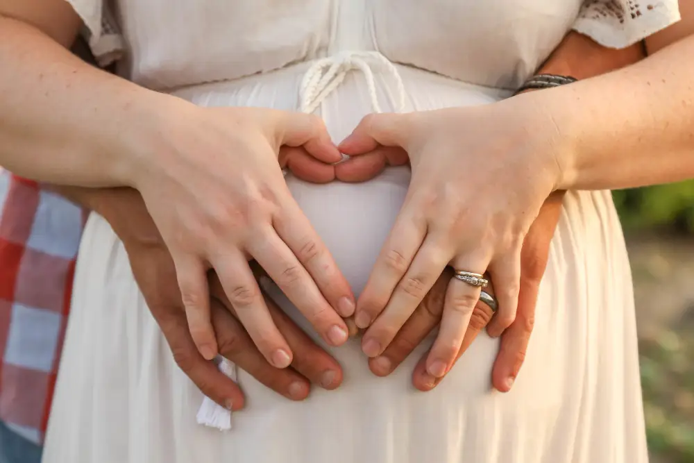 married couple forming heart shape with hands pregnant belly woman